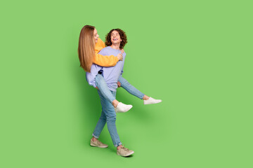 Sticker - Full length profile portrait of two carefree cheerful people piggyback cuddle walk empty space isolated on green color background