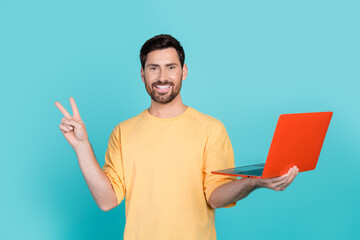 Sticker - Portrait photo of friendly young man working remote using netbook makes v sign sending greetings isolated on cyan color background