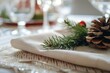 © Pinklife - A solitary pinecone rests atop a festive napkin, surrounded by elegant tableware and a delicate christmas tree, bringing the beauty of the outdoors indoors
