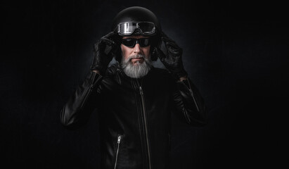 Wall Mural - Portrait d'un motard homme avec un casque noir et une veste en cuir et des lunettes de protection et une barbe grise vintage