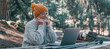 © Daniel - Head shot portrait close up of cute one of old middle age person using computer pc outdoors sitting at a wooden table in the forest of mountain in nature with trees around her..