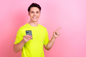 Poster - Photo portrait of nice teen man hold gadget point empty space dressed stylish yellow clothes isolated on pink color background