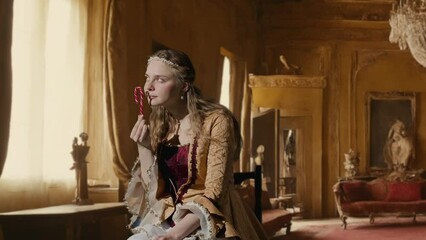 Wall Mural - Woman in ancient outfit on background of historic interior. Female in renaissance style dress sitting holding candy cane eating sweets enjoying.