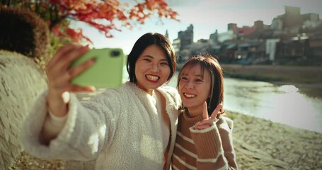 Wall Mural - Selfie, smile and japanese women at river for holiday travel, fun and happy adventure together with nature. Digital photography, peace sign and couple of friends relax on outdoor vacation in Japan.