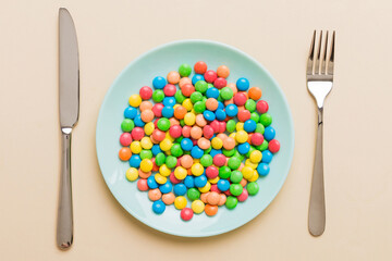 Wall Mural - cutlery on table and sweet plate of candy. Health and obesity concept, top view on colored background