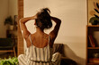 © pressmaster - Rear view of young brunette woman holding her hair while sitting on bed in front of camera and enjoying morning chill on weekend
