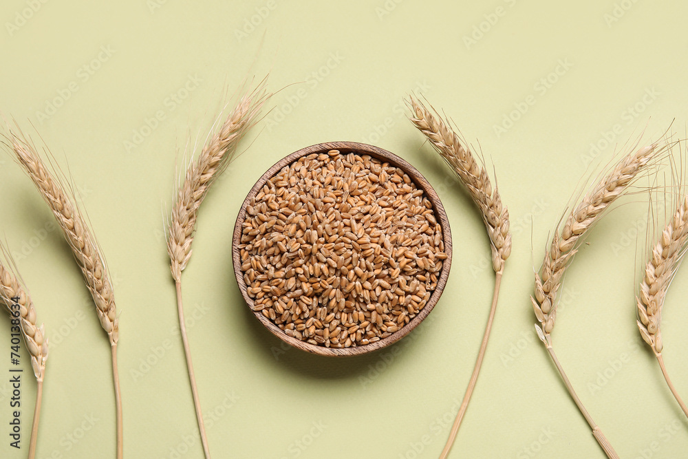 Wooden bowl with grains and wheat ears on light green background