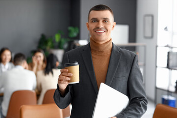 Wall Mural - Businessman with cup of coffee and laptop in conference hall