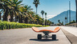 A skateboard sits idly on the side of the road, waiting for its rider. Street view with palm and lonely long board