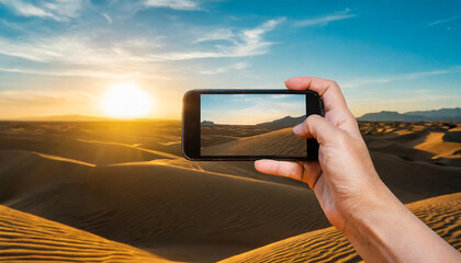 Wall Mural - Hand holding a smart phone and taking pictures of the desert at sunset