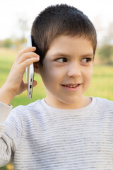 Handsome 6 year old boy talking on the phone while standing in park in autumn.