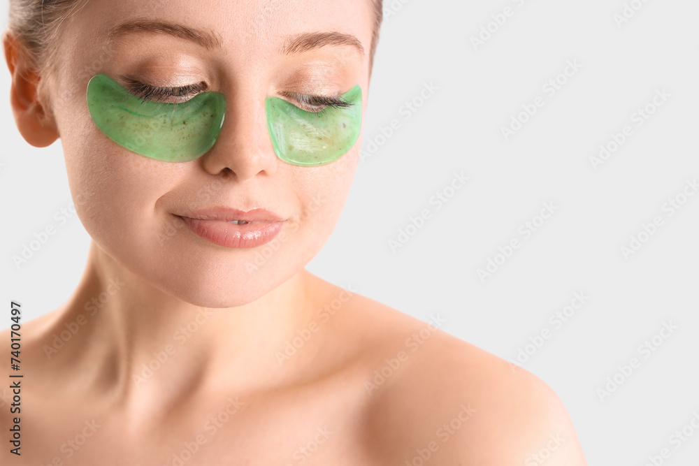 Young woman with under-eye patches on light background, closeup