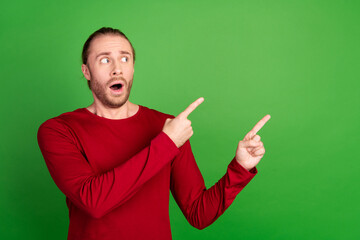 Wall Mural - Photo of astonished man with stubble dressed red pullover staring indicating at discount empty space isolated on green color background