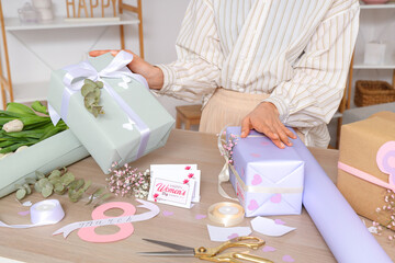 Canvas Print - Woman with beautiful gift boxes and packing materials at wooden table. International Women's Day