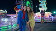 © stockbusters - Happy girls walking illuminated amusement park. Smiling best friends enjoying