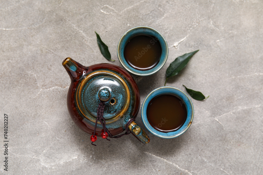 Ceramic teapot with cups of hot matcha tea on grey background