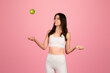 Playful young woman in white fitness attire joyfully tossing a green apple into the air