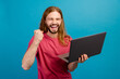 © deagreez - Portrait of overjoyed handsome guy use laptop raise fist shout yes hooray isolated on blue color background