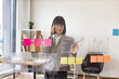 Caucasian woman in glasses talking on smartphone and looking on financial graphic on glass wall before office meeting. Female administrative manager preparing for presentation at work.