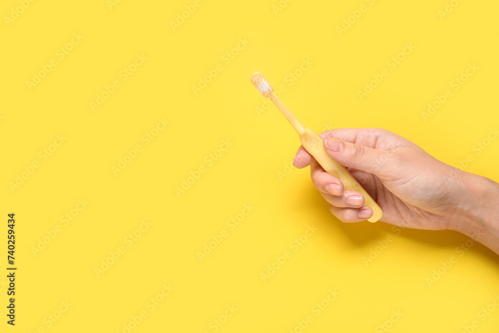 Female hand with toothbrush on yellow background.