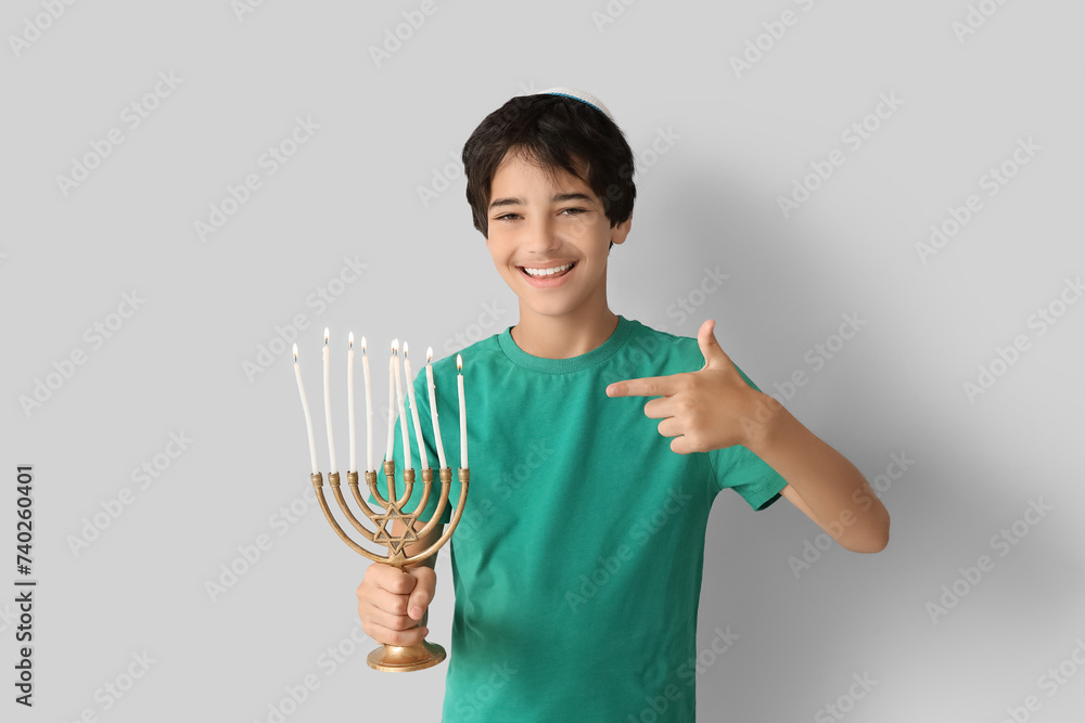 Little Israeli boy pointing at menorah on grey background