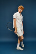 © LIGHTFIELD STUDIOS - full length of fashionable redhead man in white outfit with tennis racquet standing on blue backdrop