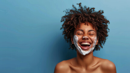 Poster - A cheerful woman with a skincare cream applied on her face is laughing with eyes closed against a blue background.