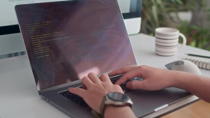 Tilt down shot of unrecognizable male programmer coding on laptop and testing on big screen