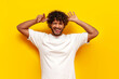 curly indian man makes faces and makes a fool of himself showing his tongue on a yellow isolated background, a young guy makes fun of and shows foolish grimaces