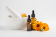 Calendula flowers in mortar and amber glass dropping bottles with essential oil. Marigold medicinal plant, herbal medicine, naturopathy and phytotherapy.