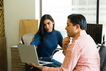 Wall Mural - Female boss helping a coworker with some of his work on a laptop computer