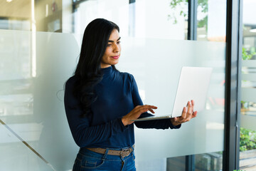 Wall Mural - Hispanic businesswoman using a laptop computer while standing in a meeting room