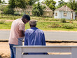 © poco_bw - african men sited on a bench next to the road talking with his friend, in the township, rondavel in the background