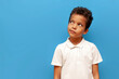 © Богдан Маліцький - african american pensive teenage boy in white polo thinks and plans on blue isolated background