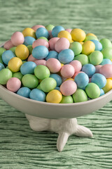 Canvas Print - Decorative white bowl held up by the Easter Bunny full of candy coated pastel easter eggs on a textured green velvet background, Happy Easter
