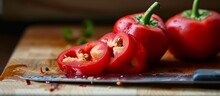 Sharp Knife And Vibrant Red Peppers Placed On A Wooden Cutting Board