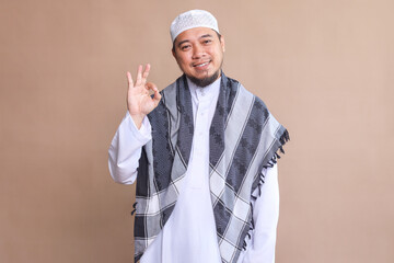 Asian muslim man feeling proud, carefree, confident and happy, smiling positively with okay hand gesture