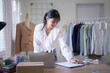© snowing12 - Young asian merchant women wearing measure tape in her neck and writing customer information in paper while checking purchase online order on laptop and working about online shopping business