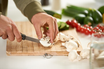 Vegetables, cooking and hands cutting mushroom on kitchen counter with salad, wellness and nutrition in home. Wood board, knife and healthy food with brunch, chef and vegan meal prep in apartment