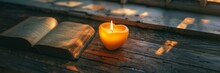 A Closed Book On A Wooden Table, Calm Light From A Nearby Heart Shaped Candle, Photo From Above.