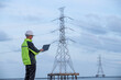© APchanel - Engineer factory electrical using a notebook computer standing at a power station planning work producing electrical energy with pole high voltage electrode background