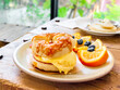 Delicious bagel with ham, cheese and egg in white dish served with blueberry and orange sliced on wooden table.