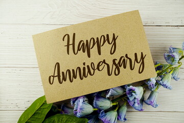 Sticker - Happy Anniversary typography text on paper card decorate with flower on wooden background