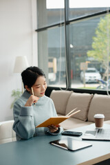 Young Asian student studying at the college library, sitting at the desk, using a laptop computer, tablet and headphones having a video chat.