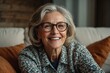 © Naveen - A cheerful, pretty older woman with elegant glasses sits on a cozy home couch, her beautiful smile lighting up the room.