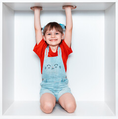 a little girl sits in a box on her lap and raises her hands up. a girl in a red t-shirt and blue sho