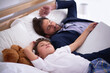 © YATrainer/peopleimages.com - Businessman, sleeping and together with child in house for comfort, relax and pyjamas to dream in bedroom. Tired, peace and dad with son on bed, cute and sweet moment for parent after work in home