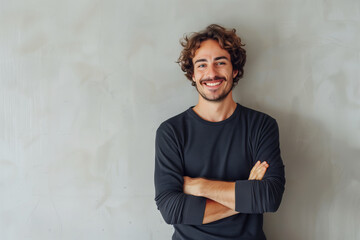 Wall Mural - Cheerful Young Man with Curly Hair Wearing a Dark Shirt Posing with Arms Crossed Against a Textured Background