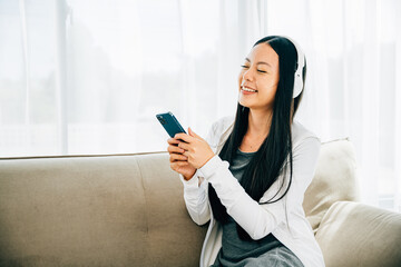 Wall Mural - Woman with smartphone and headphones relaxes on sofa listens to music. Engaged in leisure enjoyment and technology at home. Entertainment concept.