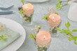 Cute easter table setting  in light colors with candles made of eggshells, green brunches, white flowers.